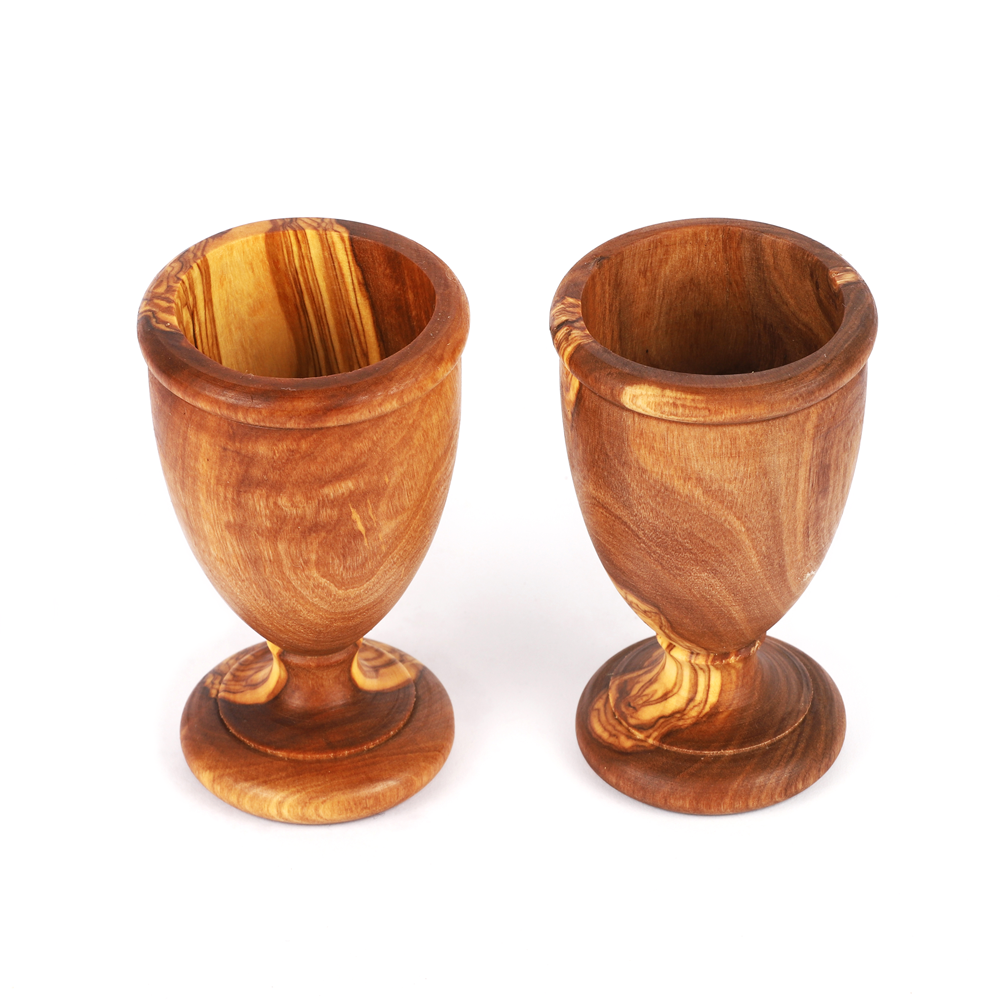 A pair of olive wood egg holders with a natural grain finish, designed to hold eggs on a breakfast table.