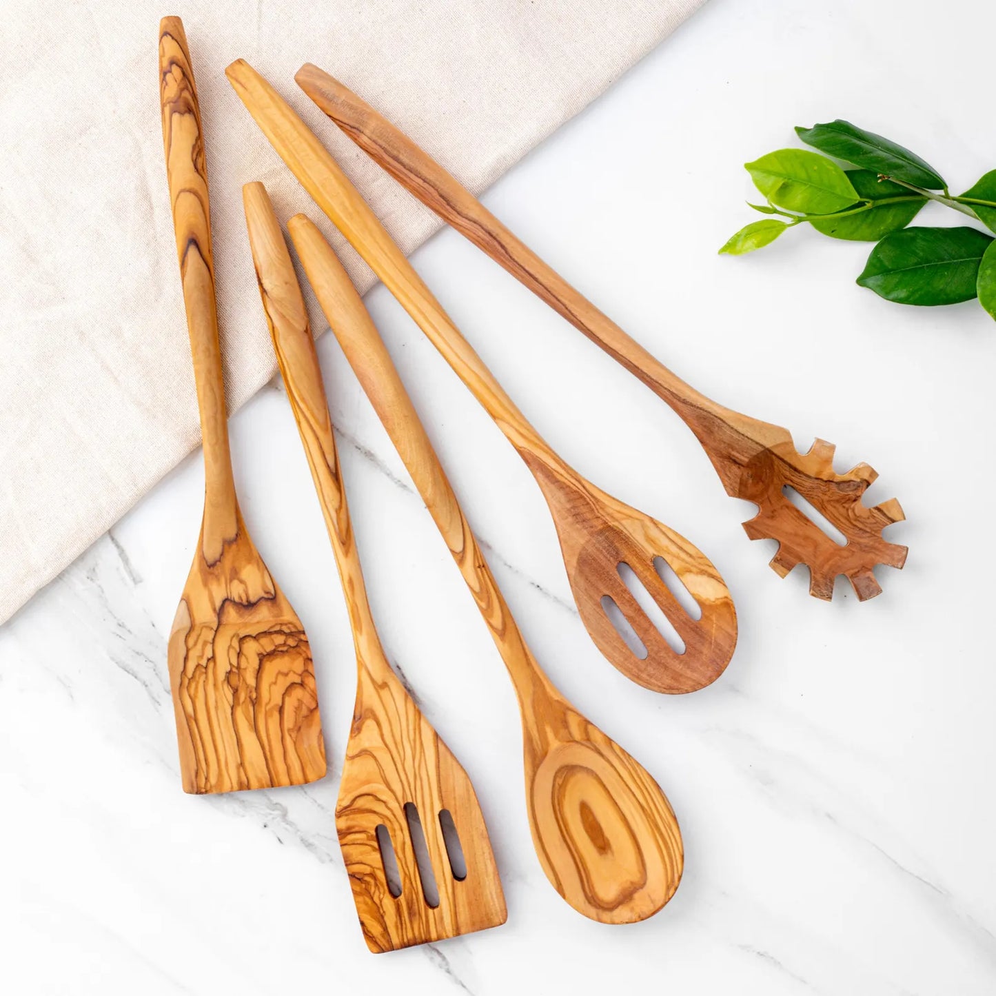 A set of five handcrafted olive wood kitchen utensils, including a ladle, spoon, fork, spatula, and turner, displayed on a marble surface.