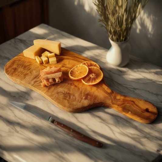 A wooden cutting board made of olive wood, displayed on a marble surface with sliced citrus and cheese, alongside a knife and a decorative vase in the background.