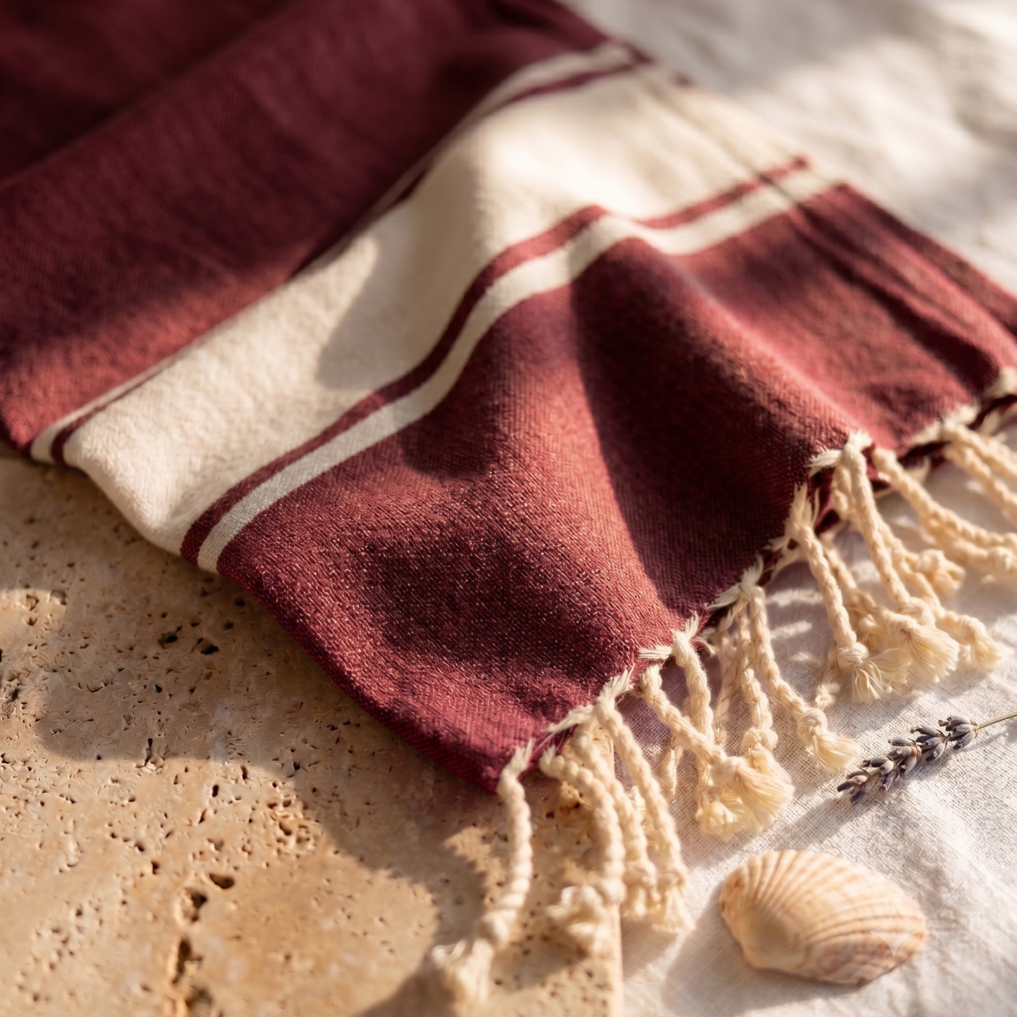 Close-up of burgundy fouta towel fabric revealing the fine cotton weave, soft texture, woven details, and handcrafted fringed edges.