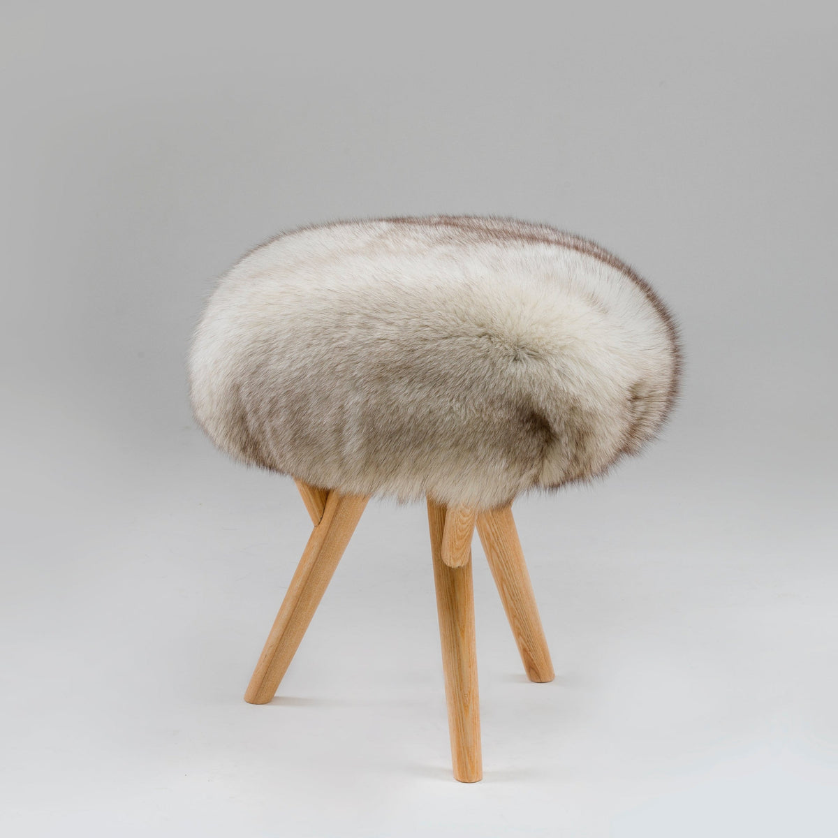 Vintage stool upholstered in genuine fox fur with handcrafted wooden legs against a grey background.