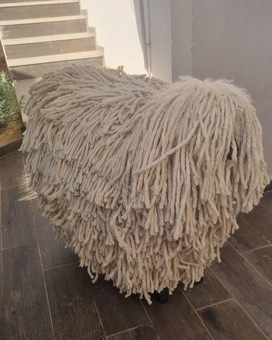 Round woven ottoman with fringed texture on a wooden floor.