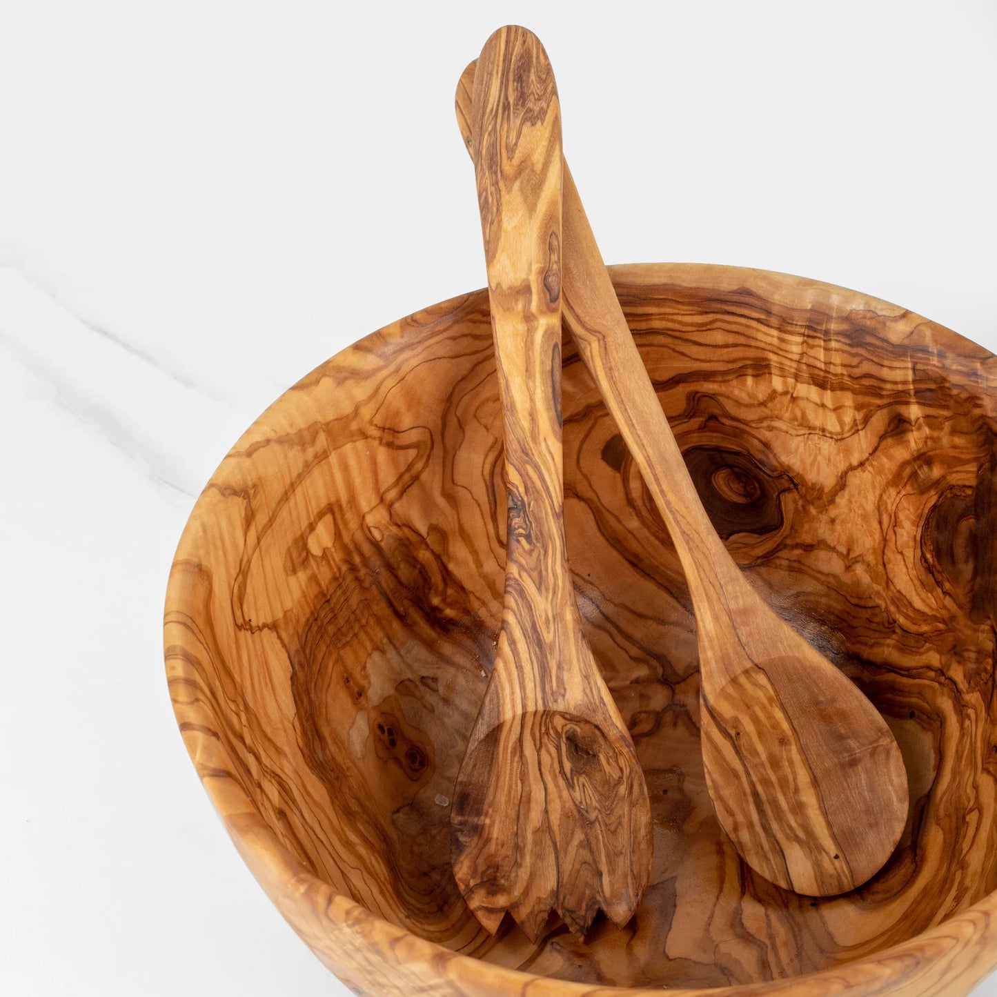 Close-up of the unique natural olive wood grain and handcrafted finish on a salad bowl and serving utensils.