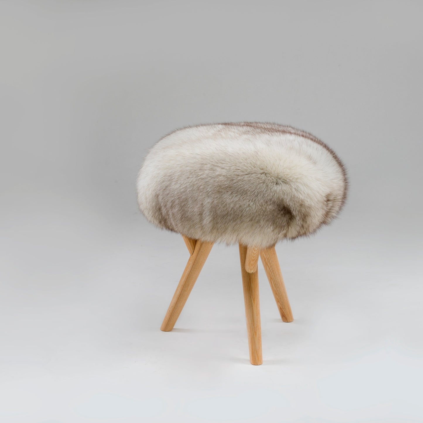 A stool with ash wood legs and a vintage fox skin seat against a grey background.